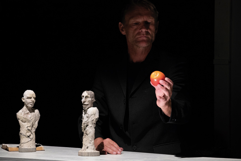 Schauspieler hält einen Apfel in der Hand. Im Vordergrund eine Figur aus einem Figurentheaterstück.