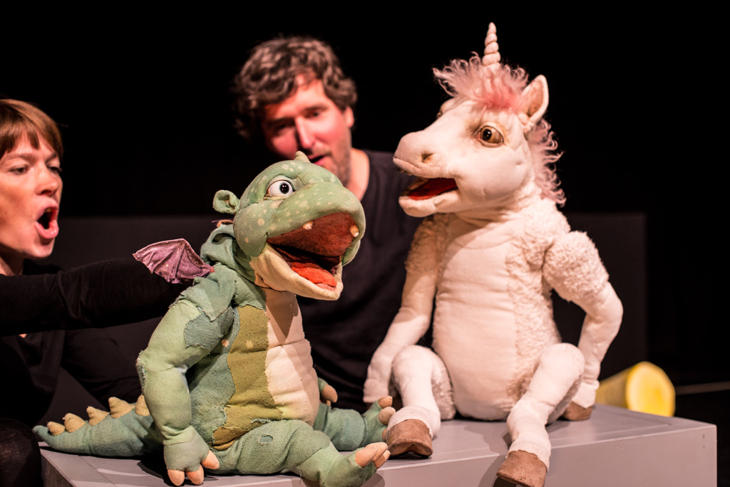 Zwei Puppenspieler mit ihren Figuren, einem Drachen und einem Einhorn in einer Szene